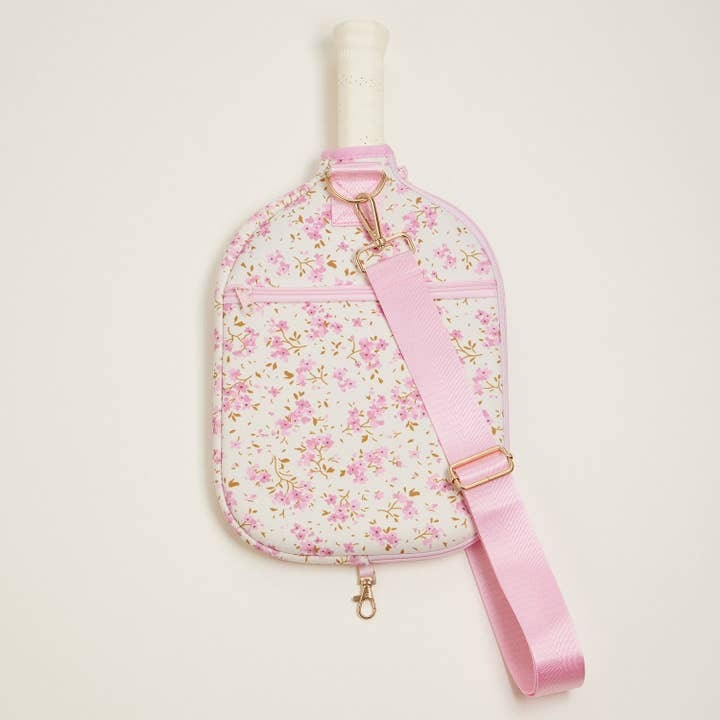 Floral-patterned sling bag with pink strap on a light beige background