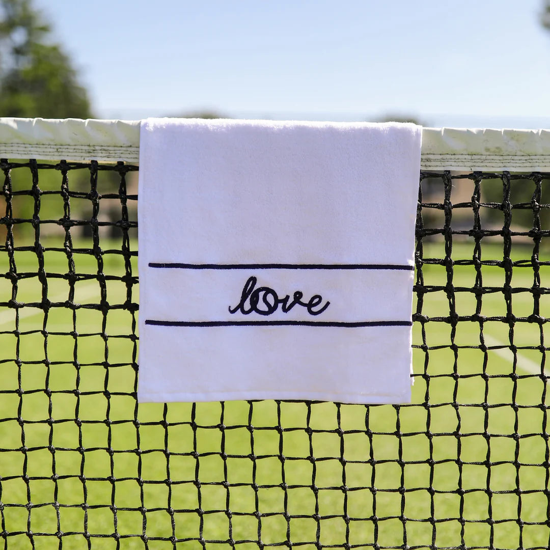 Pickleball towel that is white with navy blue letters that say "love" hanging on a tennis net