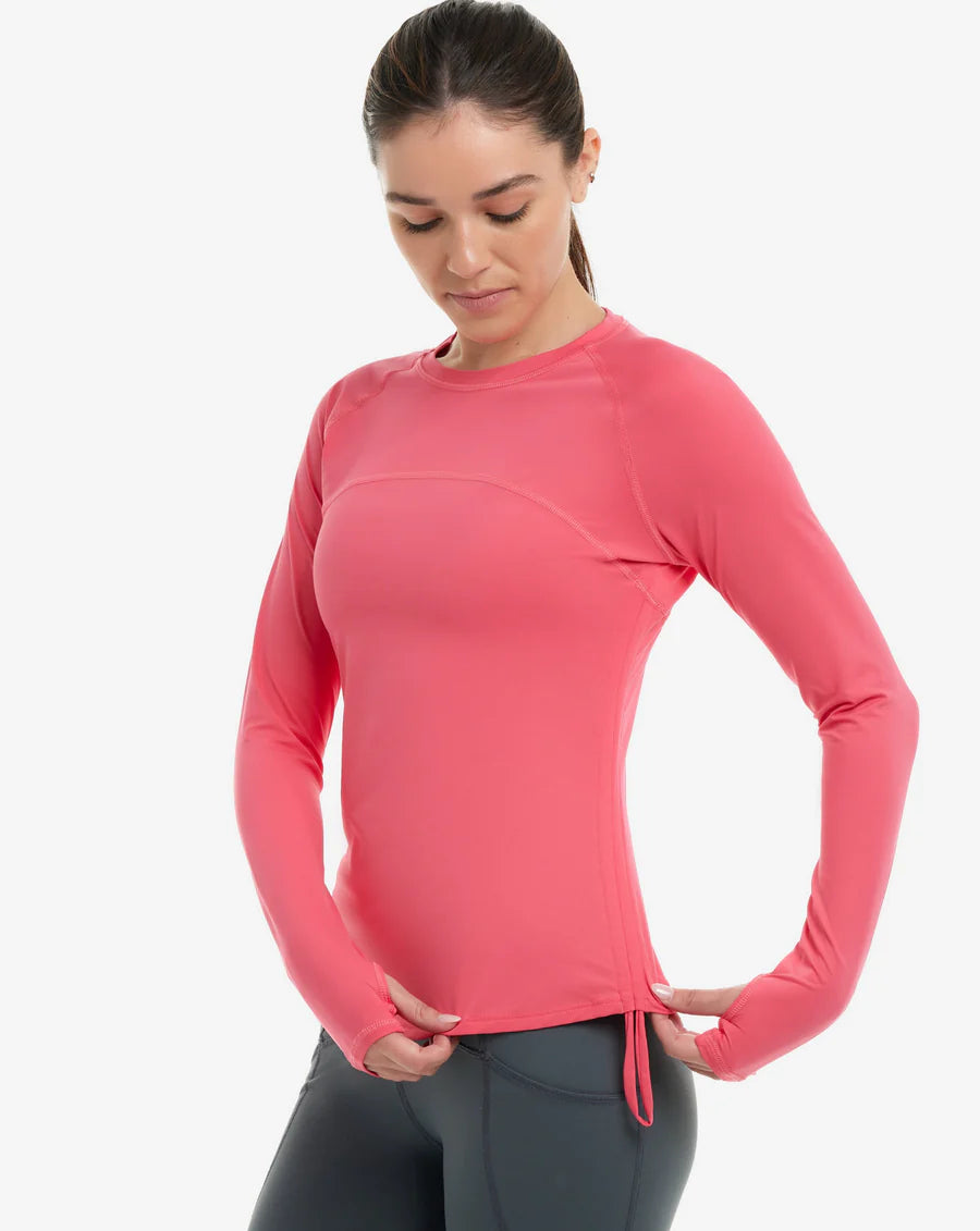 A woman wearing a coral long-sleeve UPF shirt with drawstrings, designed for sun protection.