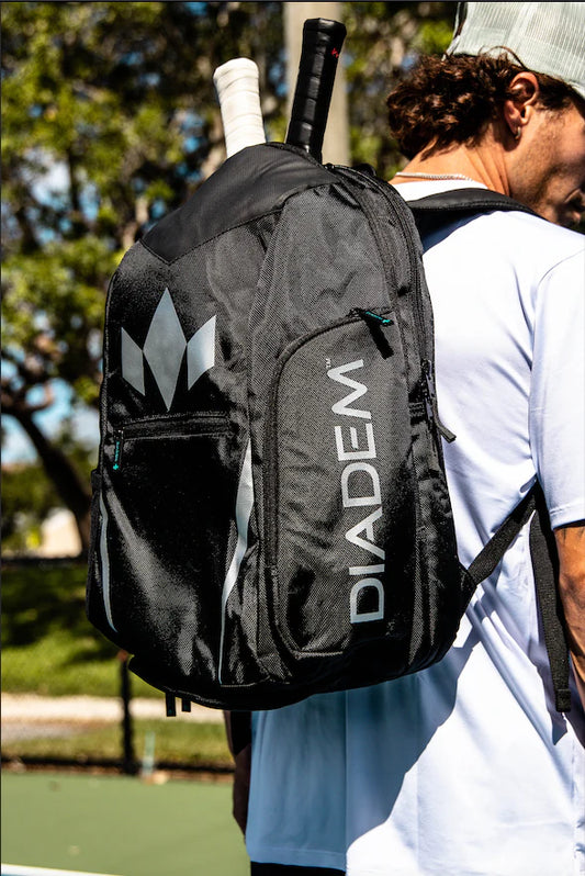 A black Diadem Tour V3 backpack designed for holding sports equipment, featuring multiple compartments and a separate shoe compartment, with a logo on the front.