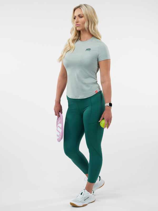Woman wearing a light gray t-shirt and green leggings holding a pink bag and a yellow ball on a white background