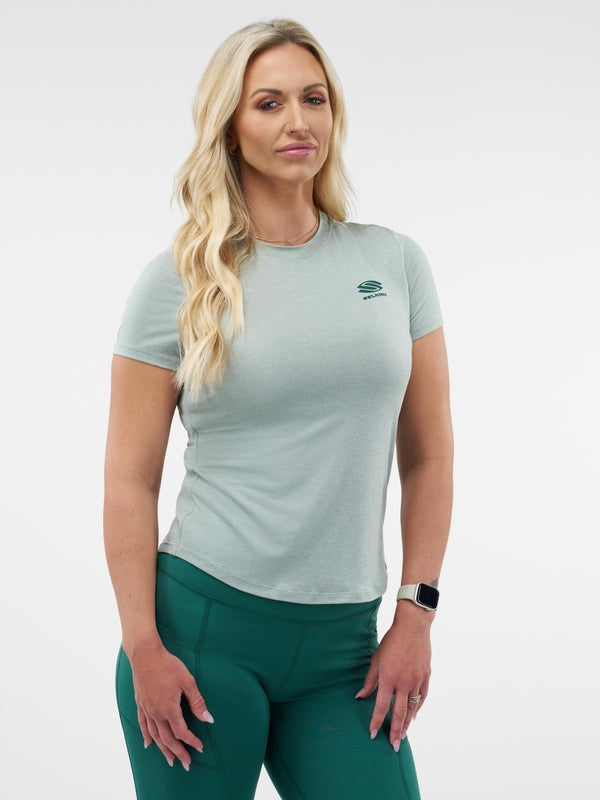 Woman wearing a light green athletic shirt and green leggings on a white background