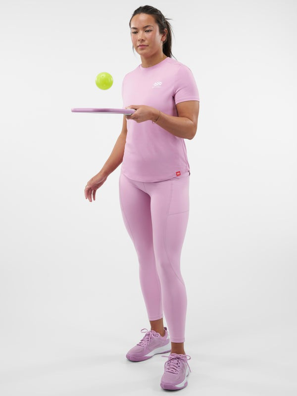 Person wearing a pink athletic outfit holding a pickleball and paddle on a white background