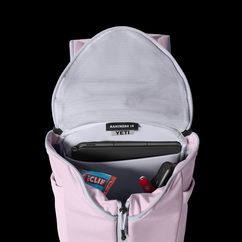 Pink backpack with open front compartment showing YETI cooler and other items on a black background