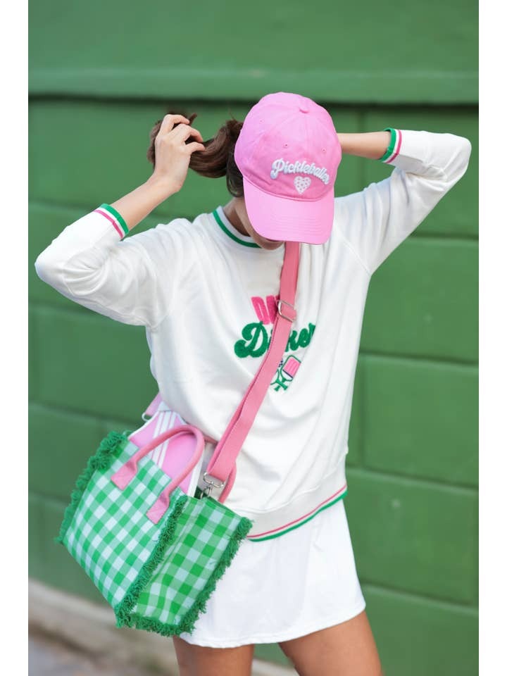 Person wearing a white sweatshirt with green accents, pink cap, and green skirt against a green background.