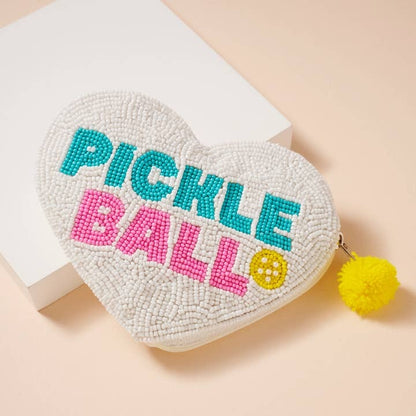 Heart-shaped beaded pouch with 'Pickle Ball' text and yellow pom-pom on a beige background
