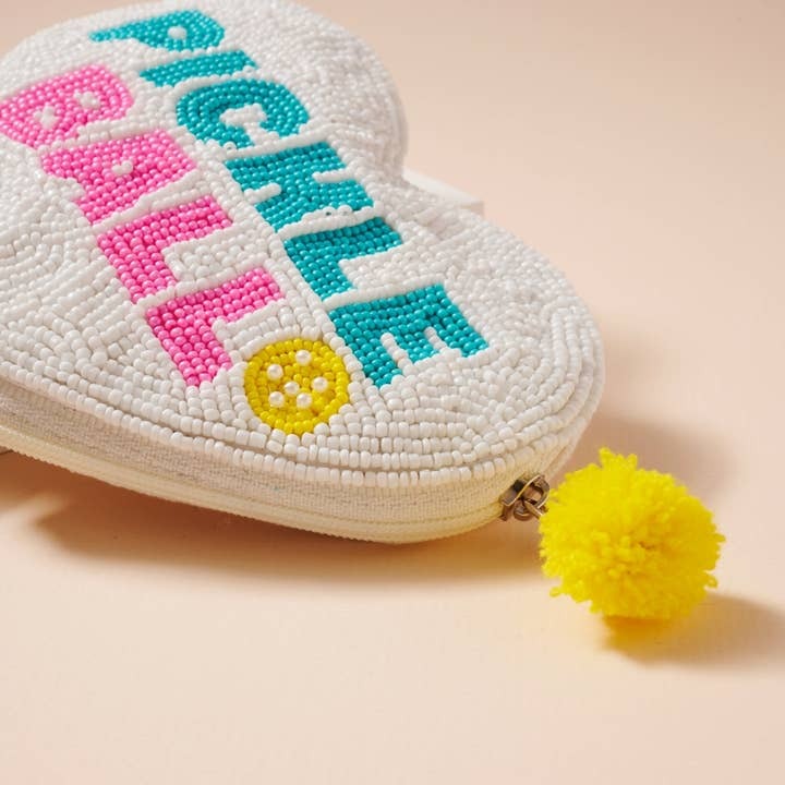 Heart-shaped beaded pouch with colorful letters and a yellow pom-pom on a beige background