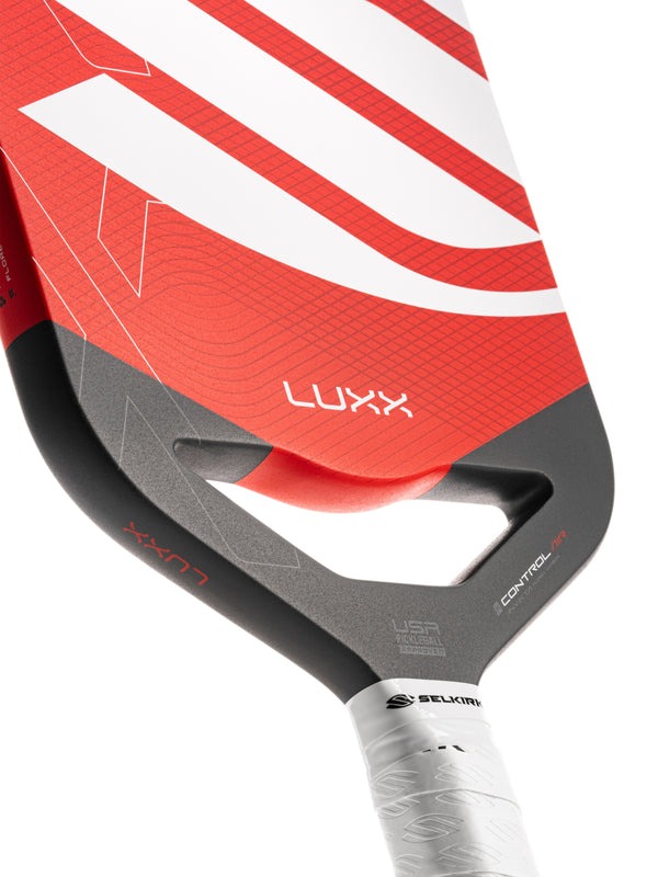 Close-up of a red and gray pickleball paddle with 'LUXX' branding on a white background.