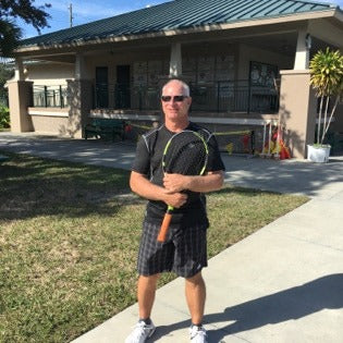 Man holding a tennis racket on a sidewalk in front of a house
