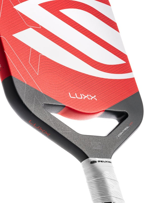 Close-up of a red and gray pickleball paddle with 'Luxx' branding on a white background