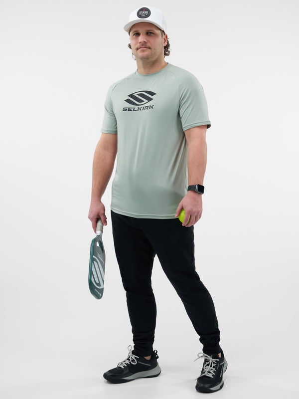 Man wearing a light gray t-shirt with a logo, holding a paddle and ball, on a white background