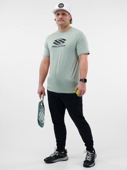 Man wearing a light gray t-shirt with a logo, holding a paddle and ball, on a white background