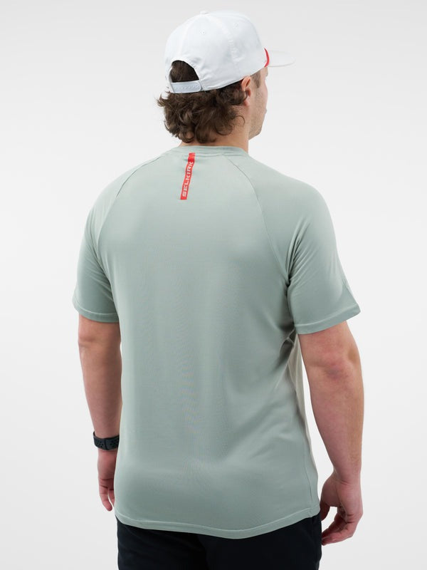 Person wearing a light gray t-shirt with a red logo on the back, standing against a white background.