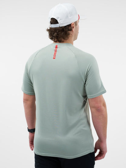 Person wearing a light gray t-shirt with a red logo on the back, standing against a white background.