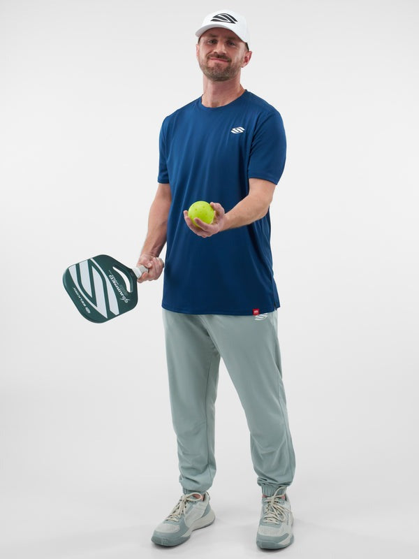 Man holding a pickleball paddle and ball against a white background
