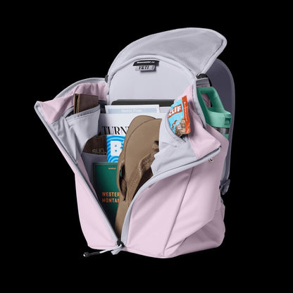 Pink backpack with items like a book and sandal inside on a black background